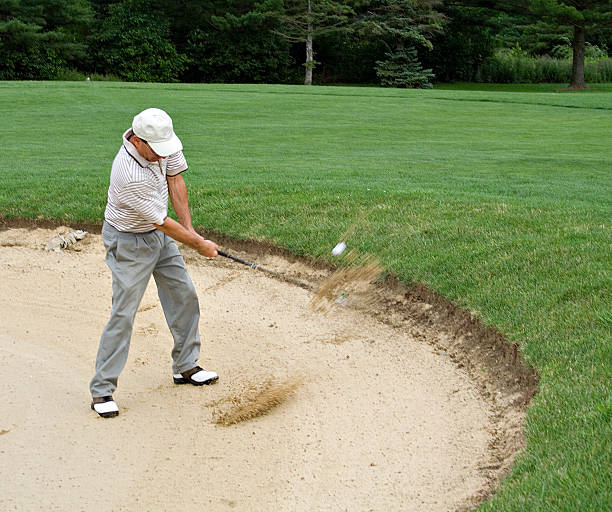 Sand and ball can be seen flying as golfer hits from sand trap.